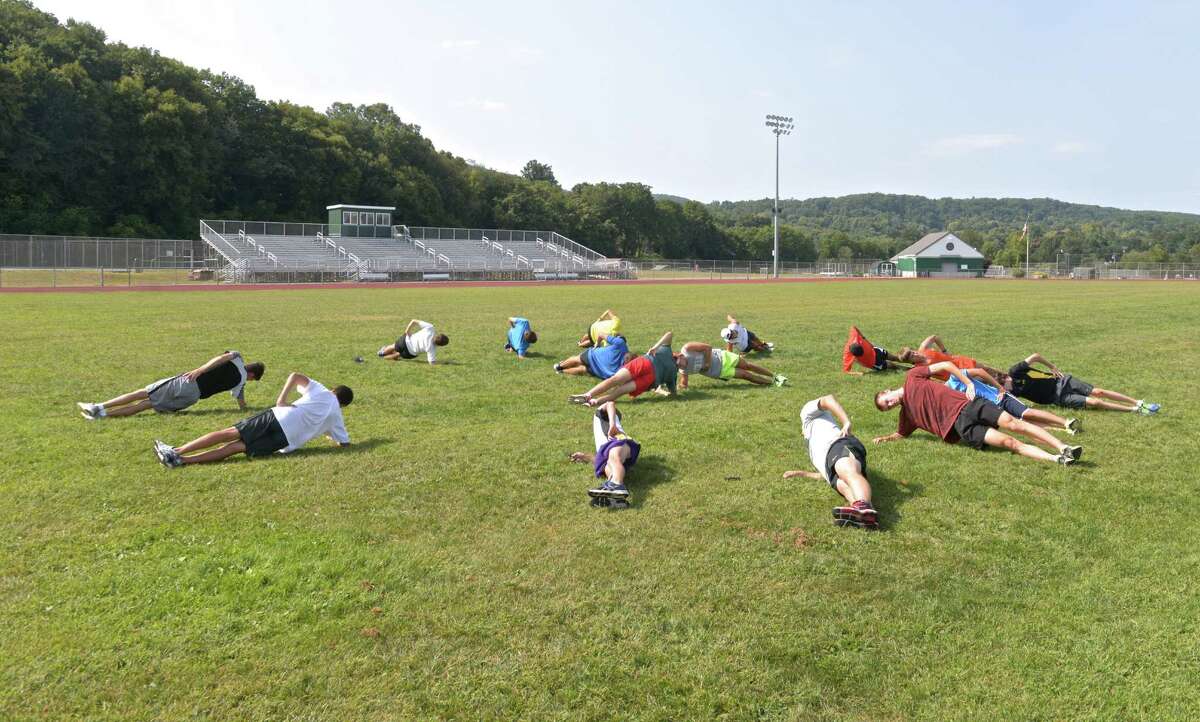 The New Milford High School cross-county team works out on the main athletic field of the high school. The Artificial Turf Construction Committee is moving ahead to install artificial turf on this and a practice field at New Milford High School.