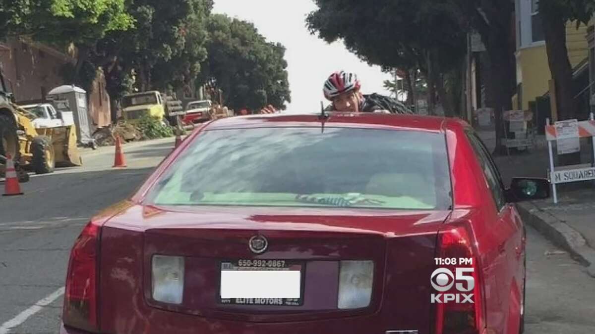 A bystander snapped this photo of cyclist Maxwell Wallace on the roof of a Cadillac that Wallace says tried to run him over in San Francisco.