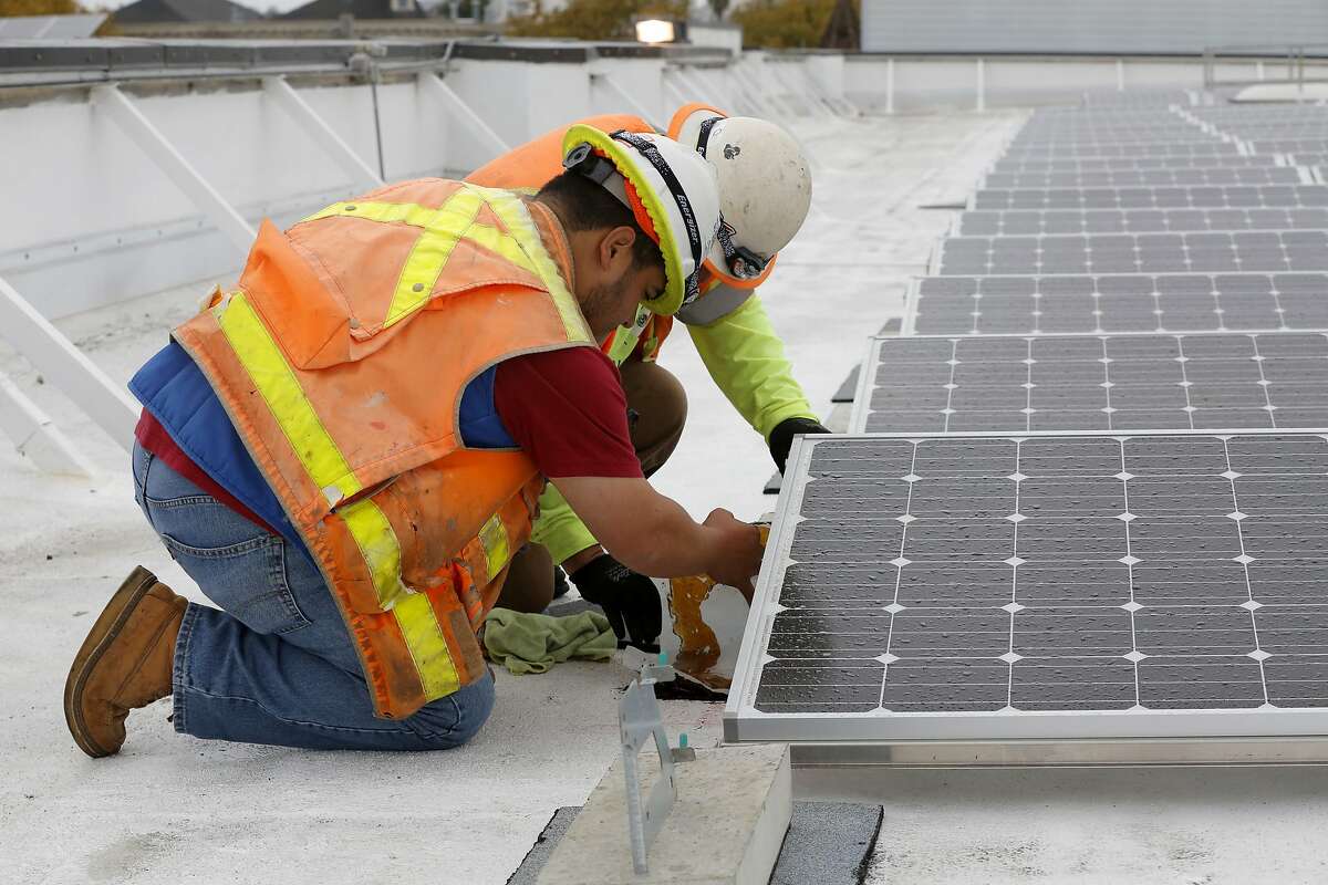 Juan Barraza (front) and Genaro Cornego anchor the seismic system for the solar panels on the roof of Cesar Chavez Elementary School in San Francisco, California, on Wednesday, Sept. 30, 2015.