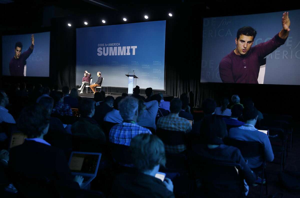 Airbnb CEO and co-founder Brian Chesky appears on the big screen during his chat with technology books publisher Tim O'Reilly at the Code for America Summit conference in Oakland, Calif. on Thursday, Oct. 1, 2015.