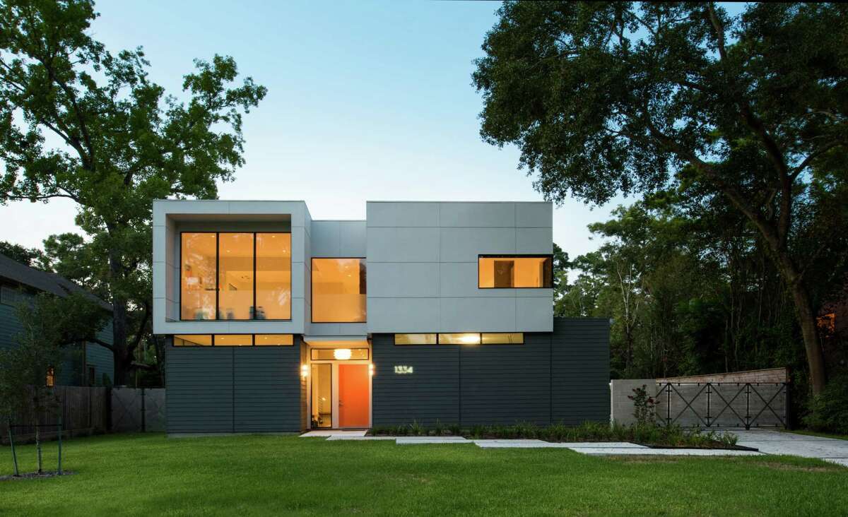 The home's exterior is decidedly modern, with a flat roof and squared-off design. The orange front door adds a pop of color to the gray and white exterior.