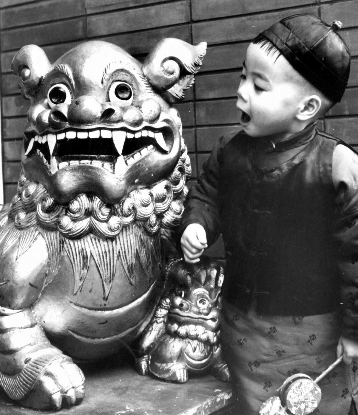 A child standing next to a lion in Chinatown is ready to celebrate the Chinese New Year in 1975. The Chinese won the right to use fireworks in the parade as part of their religion in 1908.