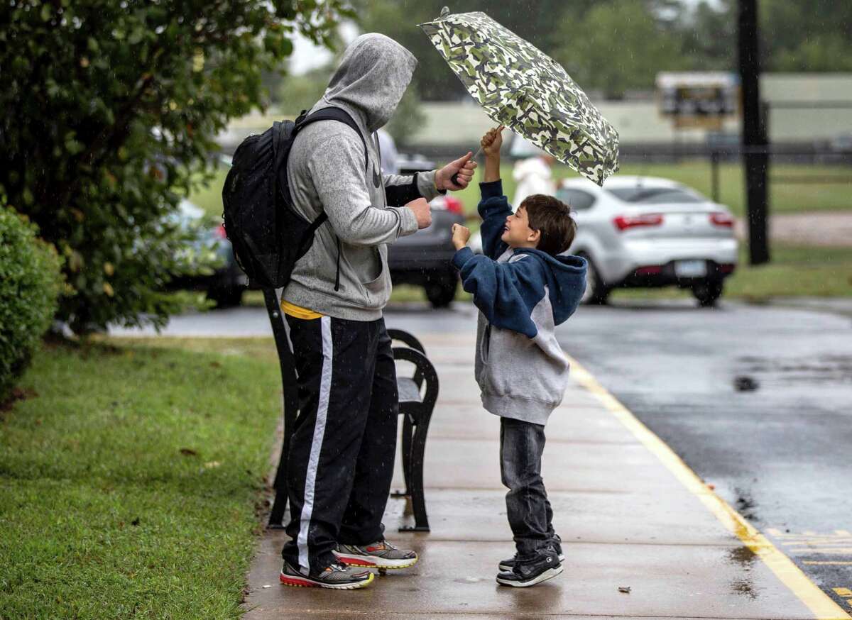 Kindergartener Jovanni Aranda, 6, right, shares his umbrella with physical education teacher Chase Davidson as he waits in Colonial Beach, Va., to be picked up after school on Friday, Oct. 2, 2015. Rain has canceled some events in the Danbury area. (Sarah Ann Jump/The Free Lance-Star via AP) MANDATORY CREDIT