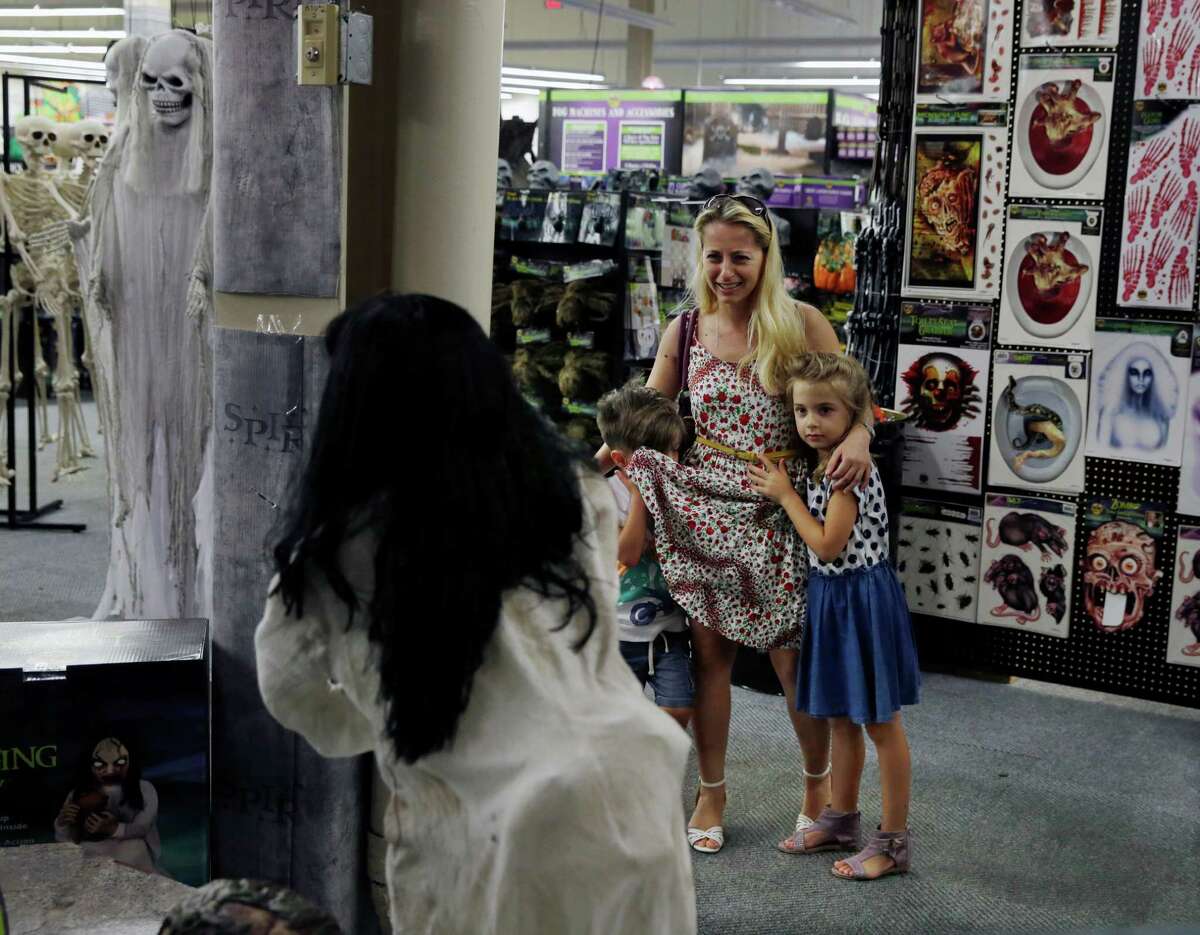 Edward Vlaicu, 4, hides his eyes as his sister Olivia Vlaicu, 6, and their mother Julia Vlaicu of Maywood, N.J., watch a moving display of zombies at a Spirit Halloween store.