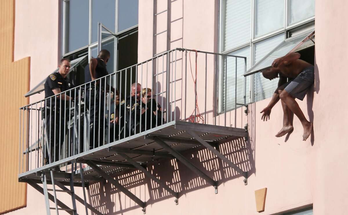 A man hangs out of a window from a building on 10th Street at Harrison Street as San Francisco Police Department officers negotiate with him from a fire escape on Wednesday, October 7, 2015 in San Francisco, Calif. A Highway Patrol spokesman said the man had been stopped while driving a white Toyota Highlander that had no license plates and when a computer check showed that the car was stolen, the man jumped to his feet and ducked into the building.