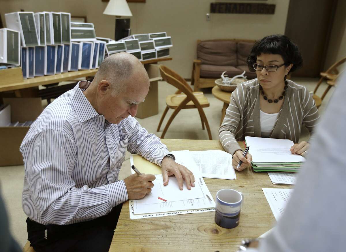 CORRECTS SPELLING OF FIRST NAME TO GRACIELA, INSTEAD OF GARCIELA - California Gov. Jerry Brown signs one of the hundreds of bills he has left to deal with as Graciela Castillo-Krings, right, his deputy legislative secretary, looks on at his Capitol office in Sacramento, Calif., Friday Oct. 9, 2015. Brown has until Sunday to either sign, veto, or just let go into law the bills passed by lawmakers in the final days of this year's legislative session. (AP Photo/Rich Pedroncelli)