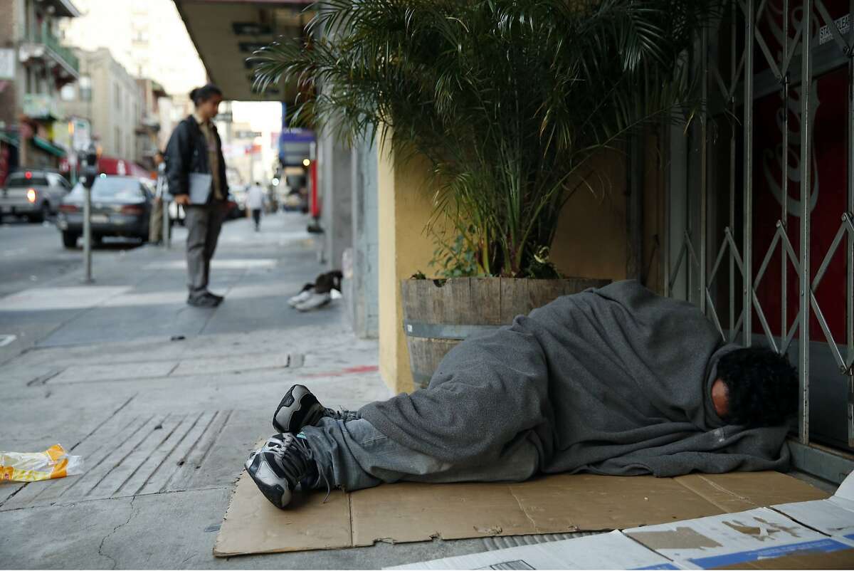 A homeless man sleeps on the sidewalk, as SF Homeless Outreach Team's Pau Liu unsuccessfully tries to convince another homeless man to relocate to the Navigation Center in San Francisco, Calif., on Tuesday, October 13, 2015.