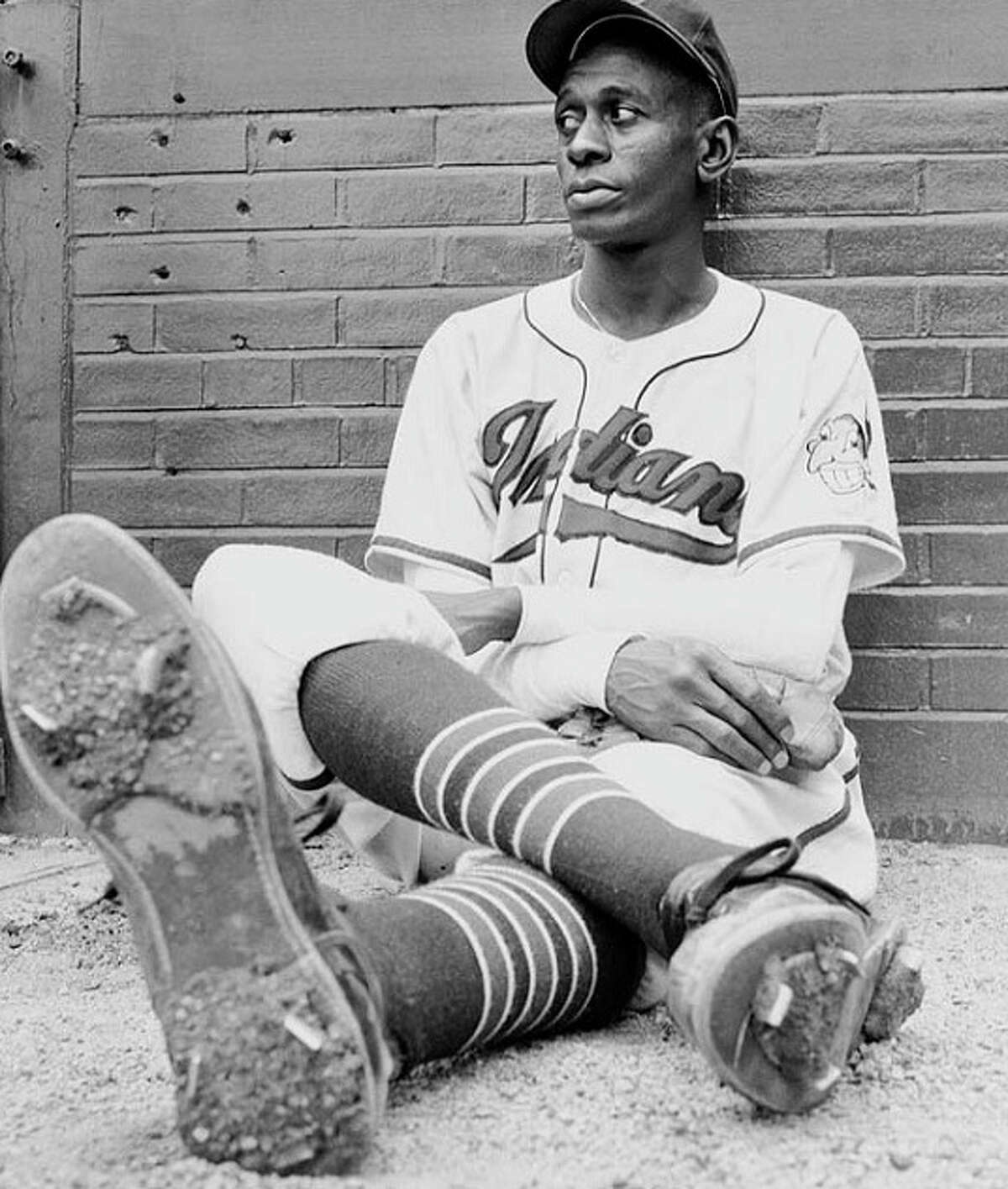 Subject: Leroy "Satchel" Paige, relief pitcher for the Cleveland Indians, extending one of his size 12 cleated shoes which inspired his nickname, while watching his teammates practice. Cleveland, Ohio July 1948 Photographer- George Silk Time Life Owned Merlin-1151918