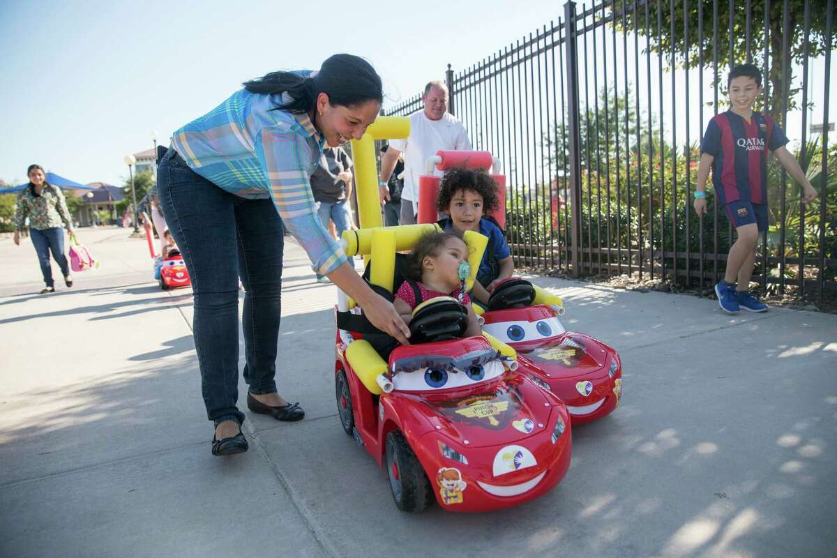 Nelly Hermosa helps her 22-month-old daughter, Leticia Vivas, steer her motorized toy car in a race during the first Go Baby Go seminar and interactive build workshop for pediatric rehabilitation patients and their families at Morgan’s Wonderland.