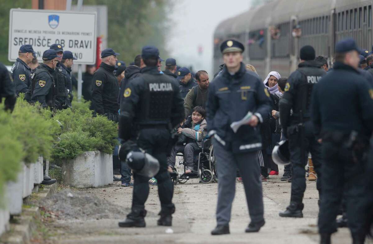 Police officers organize groups of migrants after they arrive from Croatia in Sredisce ob Dravi, Slovenia, Sunday, Oct. 18, 2015. Hungary shut down its border with Croatia to the free flow of migrants, prompting Croatia to redirect thousands of people toward its border with Slovenia. (AP Photo/Petr David Josek)