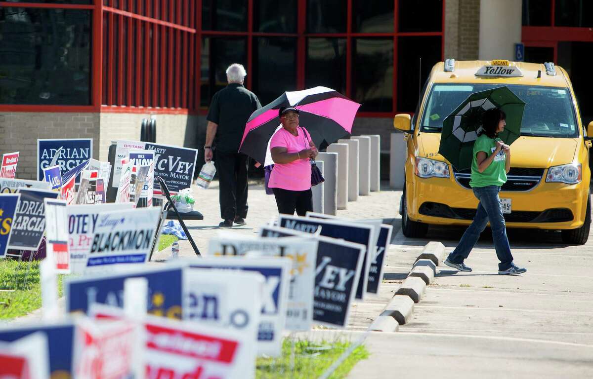Leatrix Lamberson, left, and Chris Carmona, right, stand amongst candidate signs as they hand out fliers to voters at the Metropolitan Multi-Services Center, Monday, Oct. 19, 2015, in Houston.