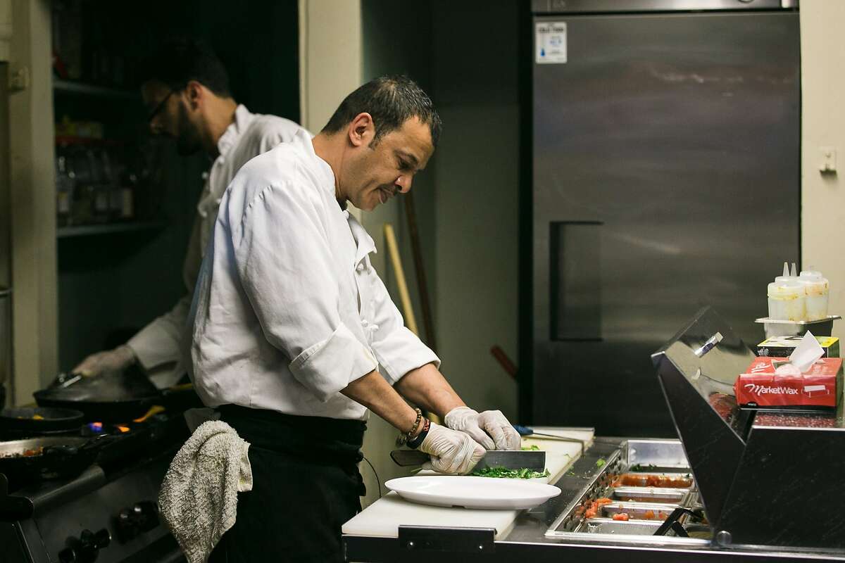 Abdul Alrammah chops cilantro while Belal Alwaqedi cooks at the girll in Yemen Kitchen.