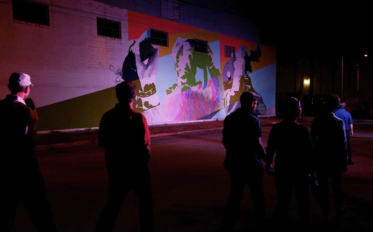 People walk past a mural by SCOTCH! on the first night of Luminaria Contemporary Arts Festival in the River North Neighborhood on Friday, Oct. 23, 2015. Despite the imminent threat of rain and storms, art patrons and a curious crowd ventured into the night to appreciate artwork spread throughout several blocks near the San Antonio Museum of Art. (Kin Man Hui/San Antonio Express-News)
