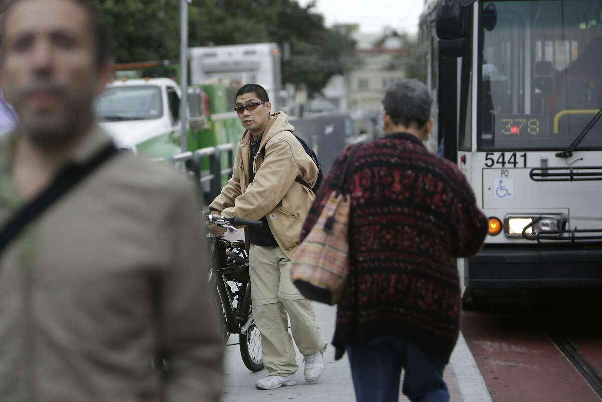 Paul Dyogi of San Francisco walks his bike at a bus stop after removing it from a bike rack on a MUNI bus on Tuesday, October 27, 2015 in San Francisco, Calif.