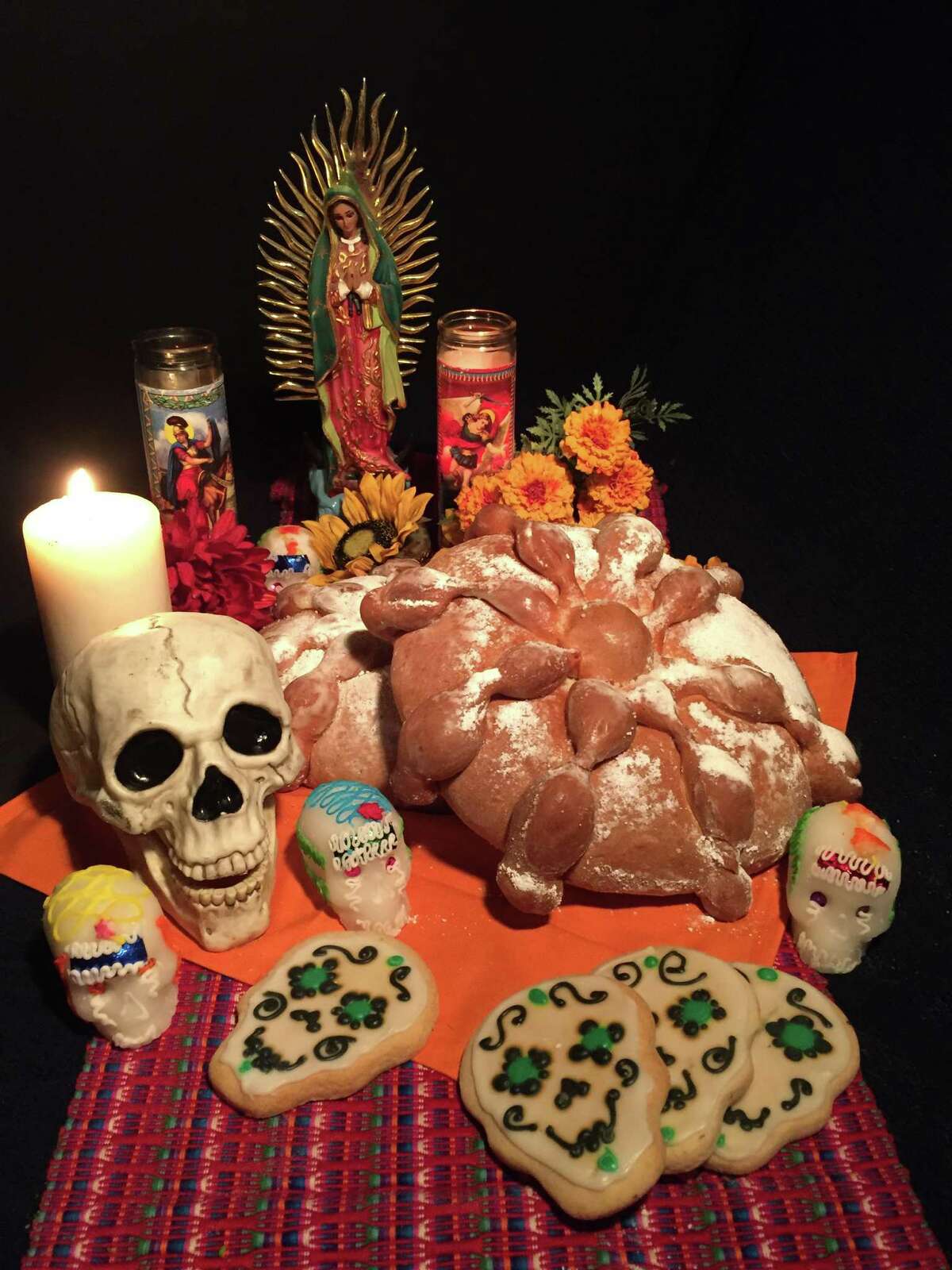 A display for Día de los Muertos: pan de muerto, candles, cookies, sugar skulls and Our Lady of Guadalupe