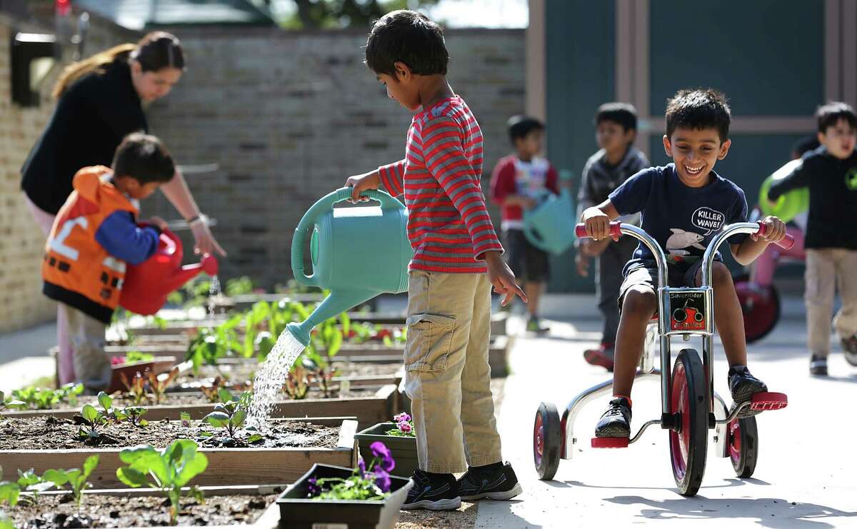 Rushil Muthyala (right) zips by on a tricycle past Sri Vibhav, who’s watering plants in the garden at Pre-K for SA North Education Center.