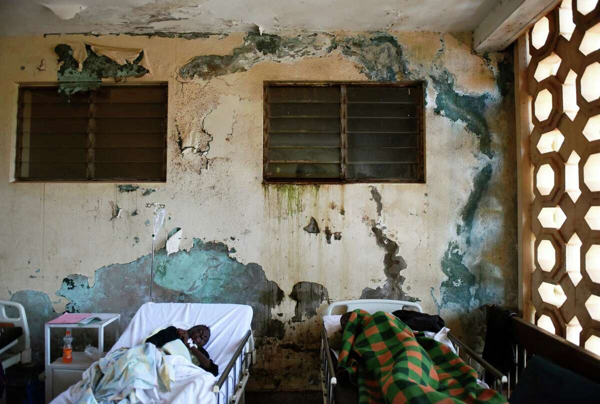 Patients lie in their beds against a wall of peeling paint in the infectious disease ward at Mulago Hospital in the capital city of Kampala, Uganda.