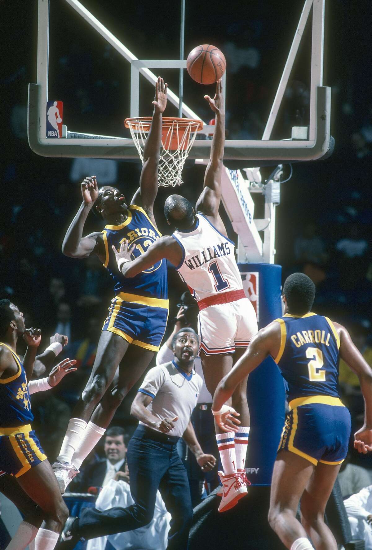 大约1985年，在马里兰州兰多弗首都中心的一场NBA篮球比赛中，华盛顿子弹队的格斯·威廉姆斯一号在金州勇士队的拉里·史密斯13号上方投篮。