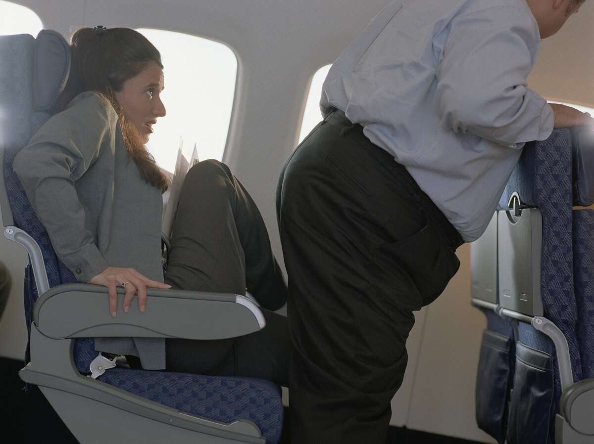 Woman sitting with her feet up on the seat giving way for a man to pass in an airplane