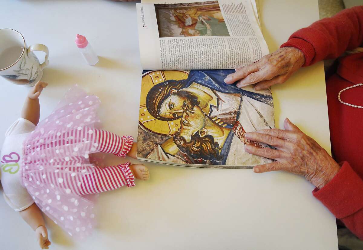 Zoila Leon, 97, flips through a magazine as she sits at the kitchen table with her caregiver Graciela Salas (not visible) as a doll her son gave her lays nearby in Leon's home Nov. 12, 2015 in San Mateo, Calif. Leon was diagnosed with Alzheimer's in 2009 and the family has been employing Graciela Salas as Leon's in-home caregiver through CareLinx since August of this year. Salas says she likes CareLinx because of the pay and their flexibility.