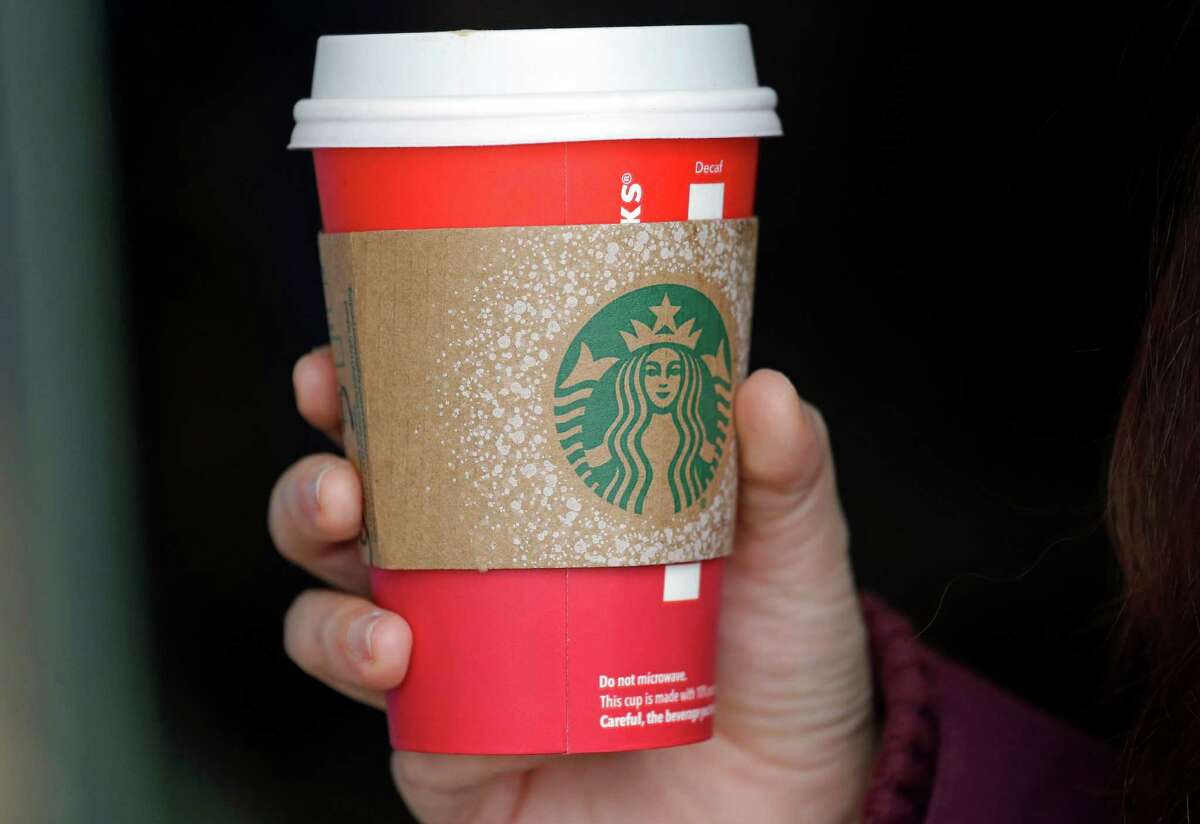 A customer carries a coffee drink in a red paper cup, with a cardboard cover attached, outside a Starbucks coffee shop in the Pike Place Market, Tuesday, Nov. 10, 2015, in Seattle. It's as red as Santa's suit, a poinsettia blossom or a loud Christmas sweater. Yet Starbucks' minimalist new holiday coffee cup has set off complaints that the chain is making war on Christmas. (AP Photo/Elaine Thompson)