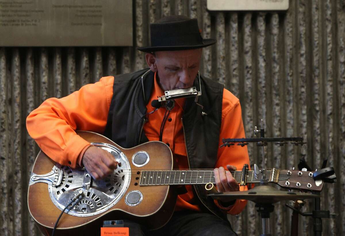 Folk musician Brian Belknap playing his harmonica and steel guitar during his afternoon session at the 16th Street BART station on November 19, 2015. He plays several instruments including the accordion, mandolin, harmonica, lap steel, slide & acoustic guitar.
