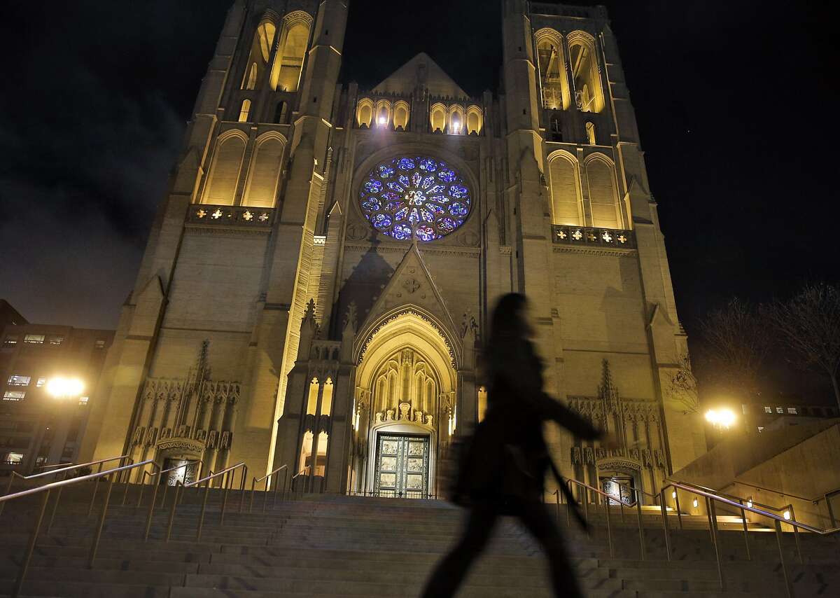 A pedestrian walks by the front of Grace Cathedral in San Francisco, Calif., on Monday, November 23, 2015. Grace Cathedral has a new look now that the stained glass rose is lighted by a daylight balanced spotlight allowing all the correct colors to be visible. In addition, two spotlights in the arcade above the rose window project colors onto the cathedral's steps.