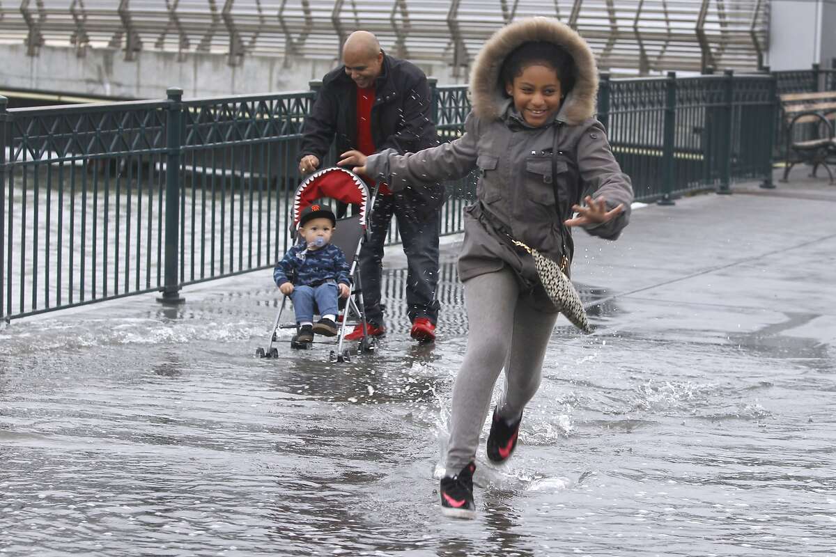 Araya Villareal dashes through water spilling onto the sidewalk with her father Isaac pushing his nephew Jamison McCall in a stroller at Pier 14 along the Embarcadero during high tide in San Francisco, Calif. on Tuesday, Nov. 24, 2015. King tide conditions are causing higher than usual water levels.