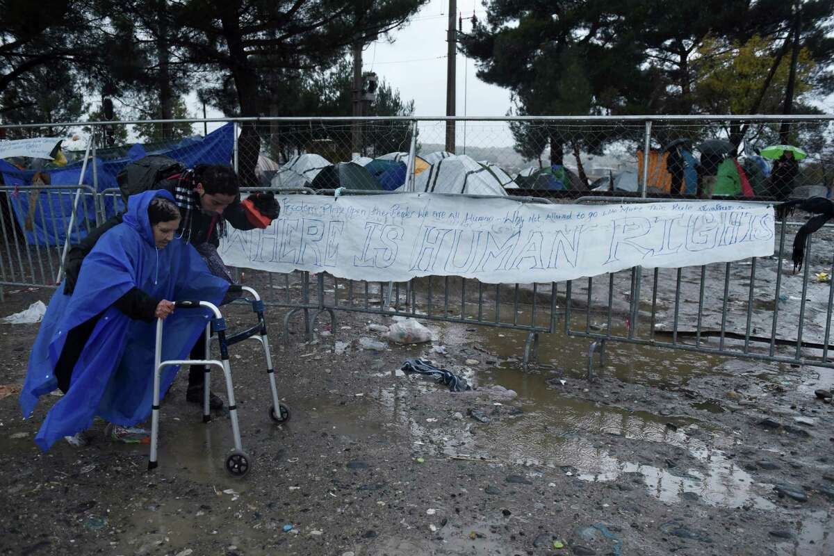 A woman is helped by another refugee to cross the Greek-Macedonian border as tents with stranded migrants are seen in no-man's land near the northern Greek village of Idomeni, Friday, Nov. 27, 2015. Macedonia toughened rules for crossings earlier this month, in the wake of the deadly Paris attacks, restricting access to citizens from countries typically granted asylum in Europe, including Syria and Afghanistan. (AP Photo/Giannis Papanikos)