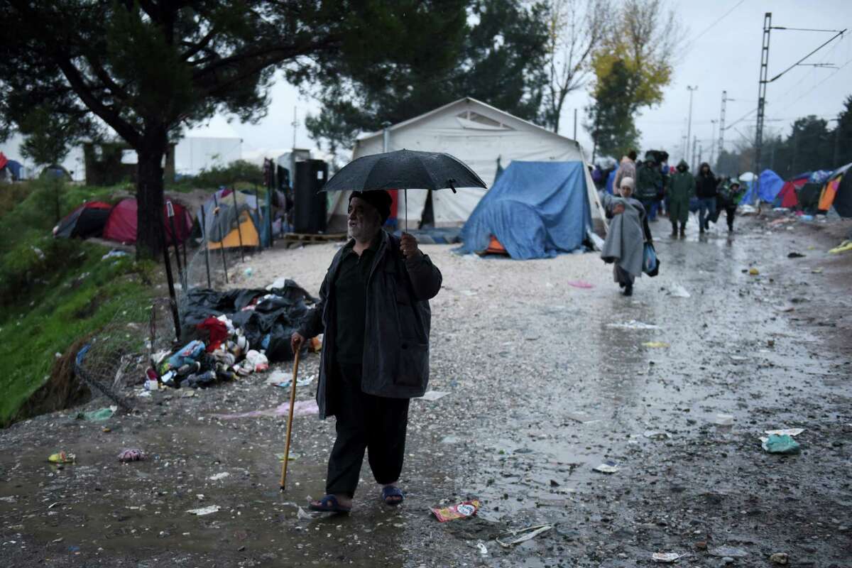 An elderly refugee walks to past the Greek-Macedonian border as tents with stranded migrants are seen in no-man's land near the northern Greek village of Idomeni, Friday, Nov. 27, 2015. Macedonia toughened rules for crossings earlier this month, in the wake of the deadly Paris attacks, restricting access to citizens from countries typically granted asylum in Europe, including Syria and Afghanistan. (AP Photo/Giannis Papanikos)