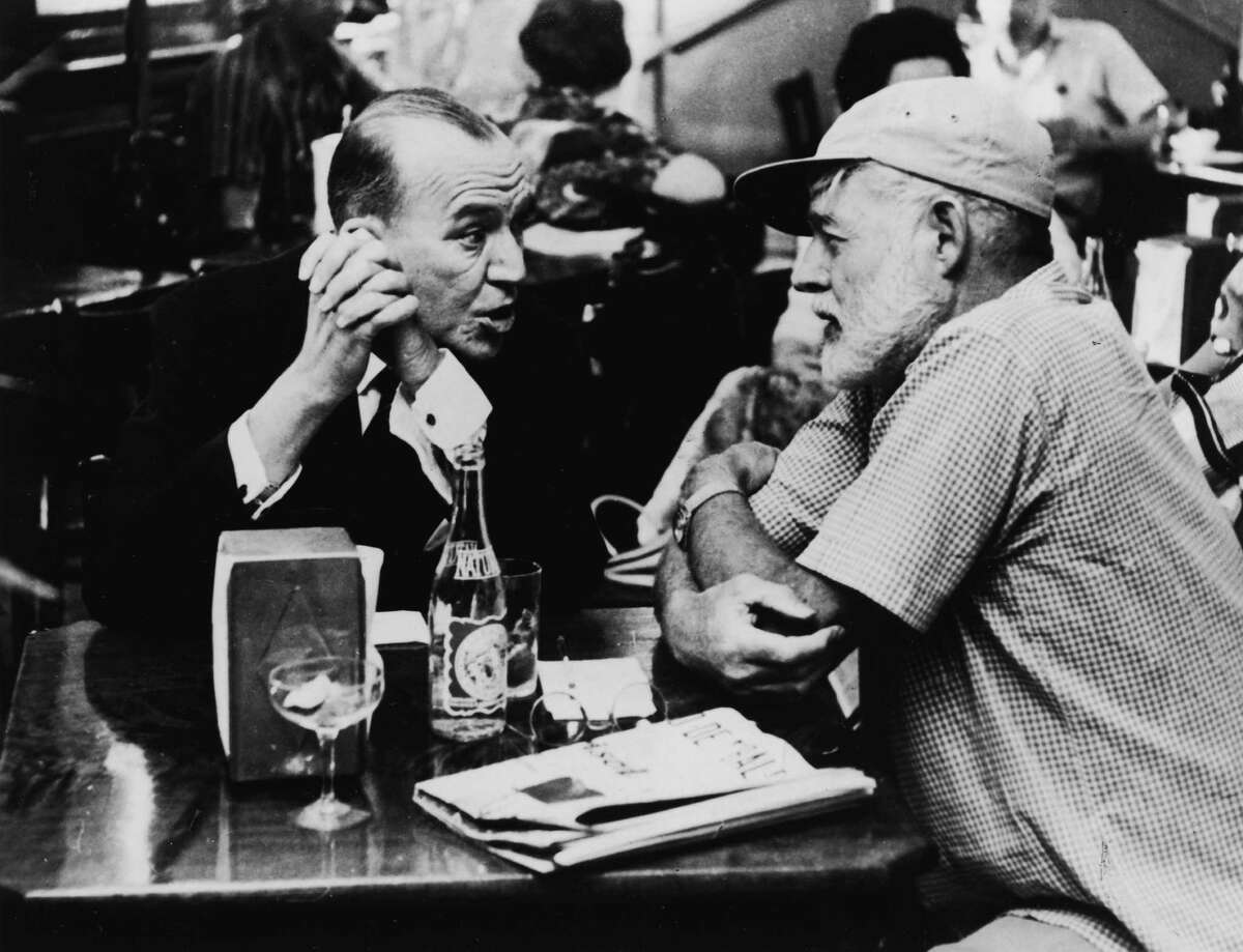 American writer Ernest Hemingway (1899 - 1961) (right) sits with his arms crossed avidly listening to British actor, playwright, and composer Noel Coward (1899 - 1973) at Sloppy Joe's Bar in Havana, Cuba, April 1, 1959. Coward was on a break from filming 'Our Man From Havana'.