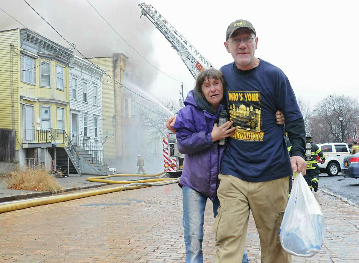 Anna Burbridge and James Blair walk away from their engulfed home on Park Ave. with a bag of belongings as firefighters fight a fire at three structures Wednesday Dec. 2, 2015 in Albany, N.Y. Burbridge and Blair were recently homeless until they moved into their apartment in the background. James said he had just made his first payment on the rent. (Lori Van Buren / Times Union)