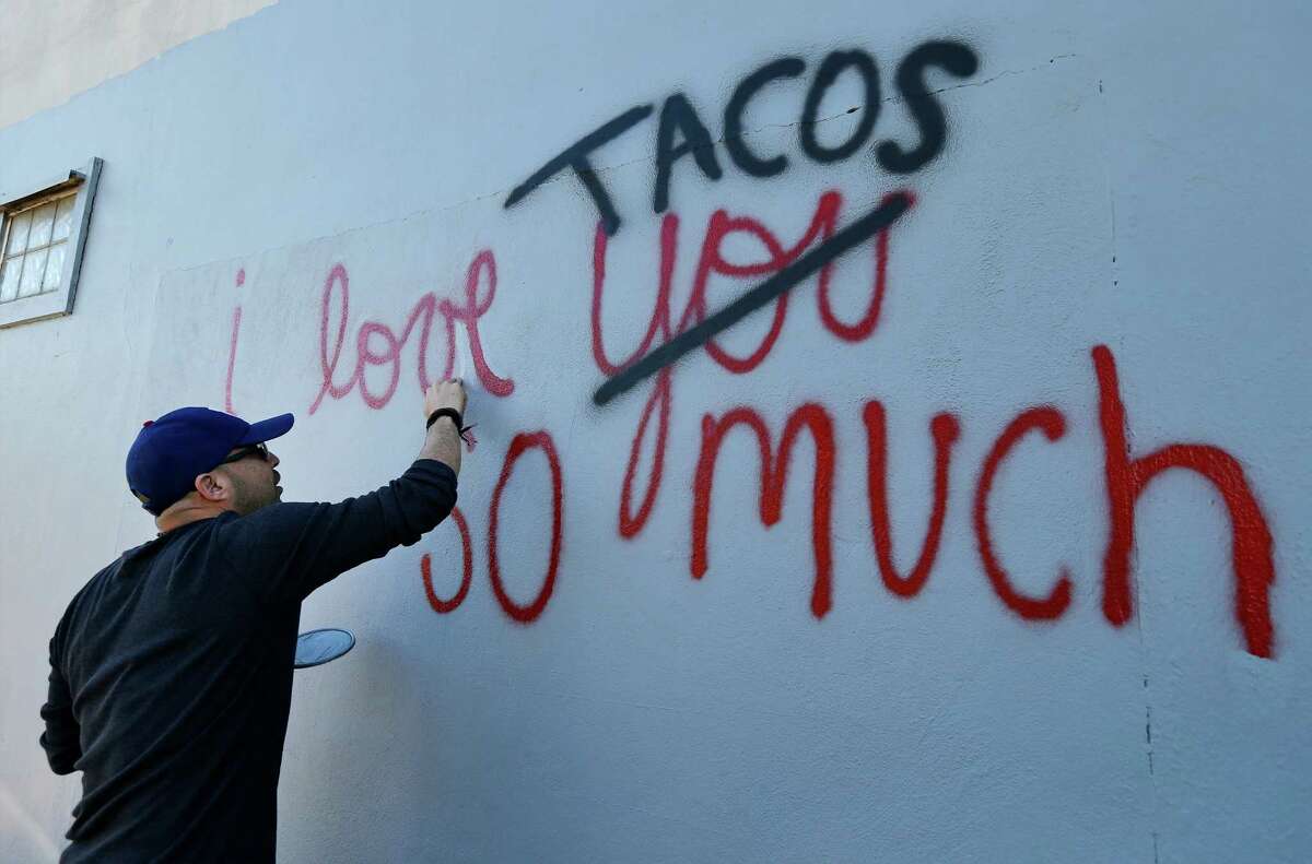 Luis Munoz touches up his artwork "I love tacos so much" which gained social media attraction earlier in the week after it was accidentally painted over by the city on Thursday, Dec. 3, 2015. After city employees were informed of their mistake, they supplied Munoz with paint and he went back to the now gray wall to remake his ode to the city and to tacos. Dozens of people who were informed of the incident via social media turned out to show their support as he re-created his art on the wall. Munoz created the artwork partly as an homage to a mural he saw in Austin and partly due to his love for tacos and the city. When social media took notice, Munoz decided to dedicate his artwork to charity whenever someone reposted his work. He was relieved to re-create his work of art but was also saddened that his original was no longer visible. However, his new homage still garnered attention from social media as well as by-passers who stopped for photos.