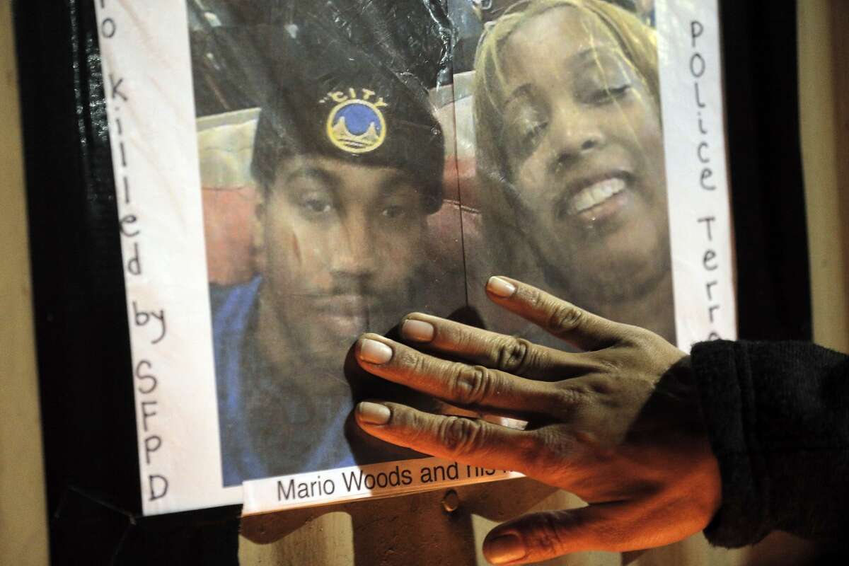 A hand reaches out to touch a photo of Mario Woods and his mom, Gwen Woods, at the site where Mario Woods was shot and killed by San Francisco Police to commemorate the young man in the Bayview district of San Francisco, Calif., on Thursday, December 3, 2015.