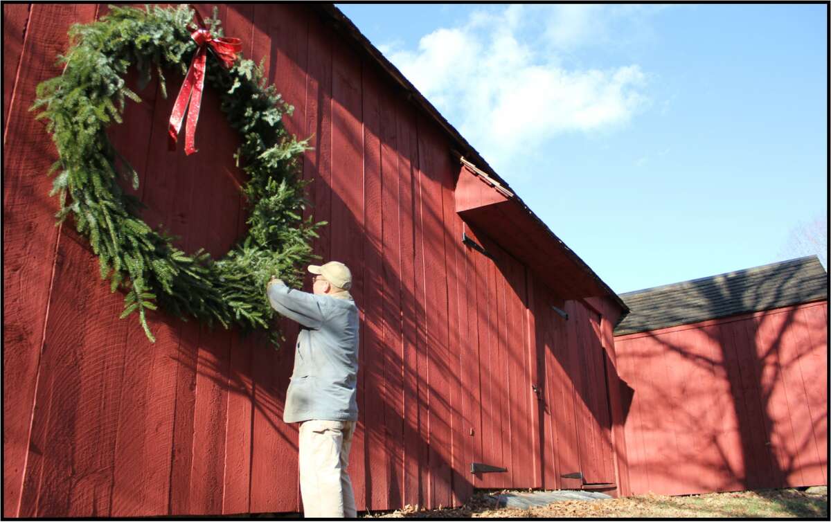 Benjamin Stiles adjusts a giant wreath hung on a barn built in 1690 on his Ragland Farm in Southbury.