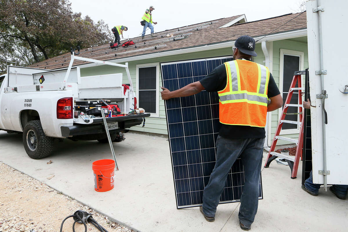 Rene Cazares (from right) with The Renewable Republic, a local solar installer, holds a solar panel as Tony Melellin and Logan Roerig make final preparations before installing it under a new program at the home of Myra Garcia on Thursday. Garcia's home is the first in San Antonio to receive a free solar system from PowerFin Partners in the SolarHostSA program.