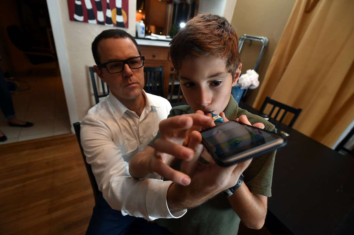 Dr. Michael Greenberg (L) demonstrates how to use his "smart" thermometer on his son Sam Greenberg (R) at their home in Berkeley, California on Friday, December 11, 2015. Kinsa Health makes the device which uses an app to track temperatures and other symptoms to help identify outbreaks of the flu or other ailments.