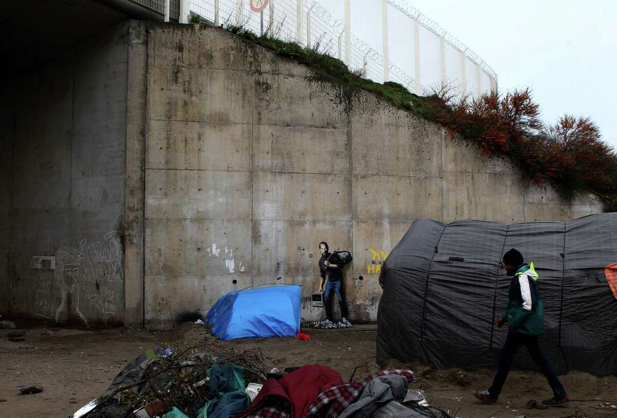 A painting by English graffiti artist Banksy is seen at the entrance of the Calais refugee camp in France, Saturday, Dec. 12, 2015. Street artist Banksy has taken on the migrant crisis in a new mural at a migrant camp in France. The elusive graffiti artist has depicted the late Apple guru Steve Jobs â?” whose biological father was from Syria â?” carrying a black garbage bag and an early model of the Macintosh computer. His publicist, Jo Brooks, confirmed Saturday that the work found at the encampment in Calais is genuine. (AP Photo/Michel Spingler)