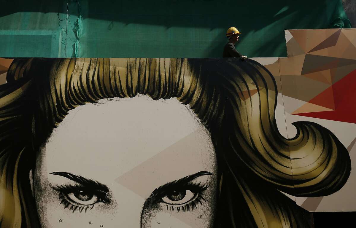 A worker stands near a commercial advertising board for a new apartment at a construction site in Hong Kong, Tuesday, Dec. 15, 2015. 