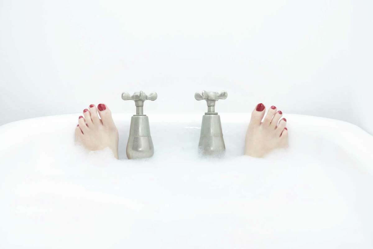 Woman in bubble bath, close-up of feet by taps
