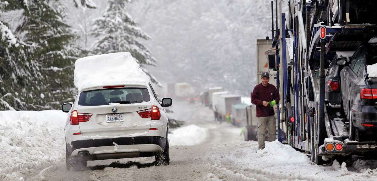A car still topped by snow drives down an onramp and past trucks stopped to remove chains after making the drive across Snoqualmie Pass, Wash., Tuesday, Dec. 22, 2015. (AP Photo/Elaine Thompson) 