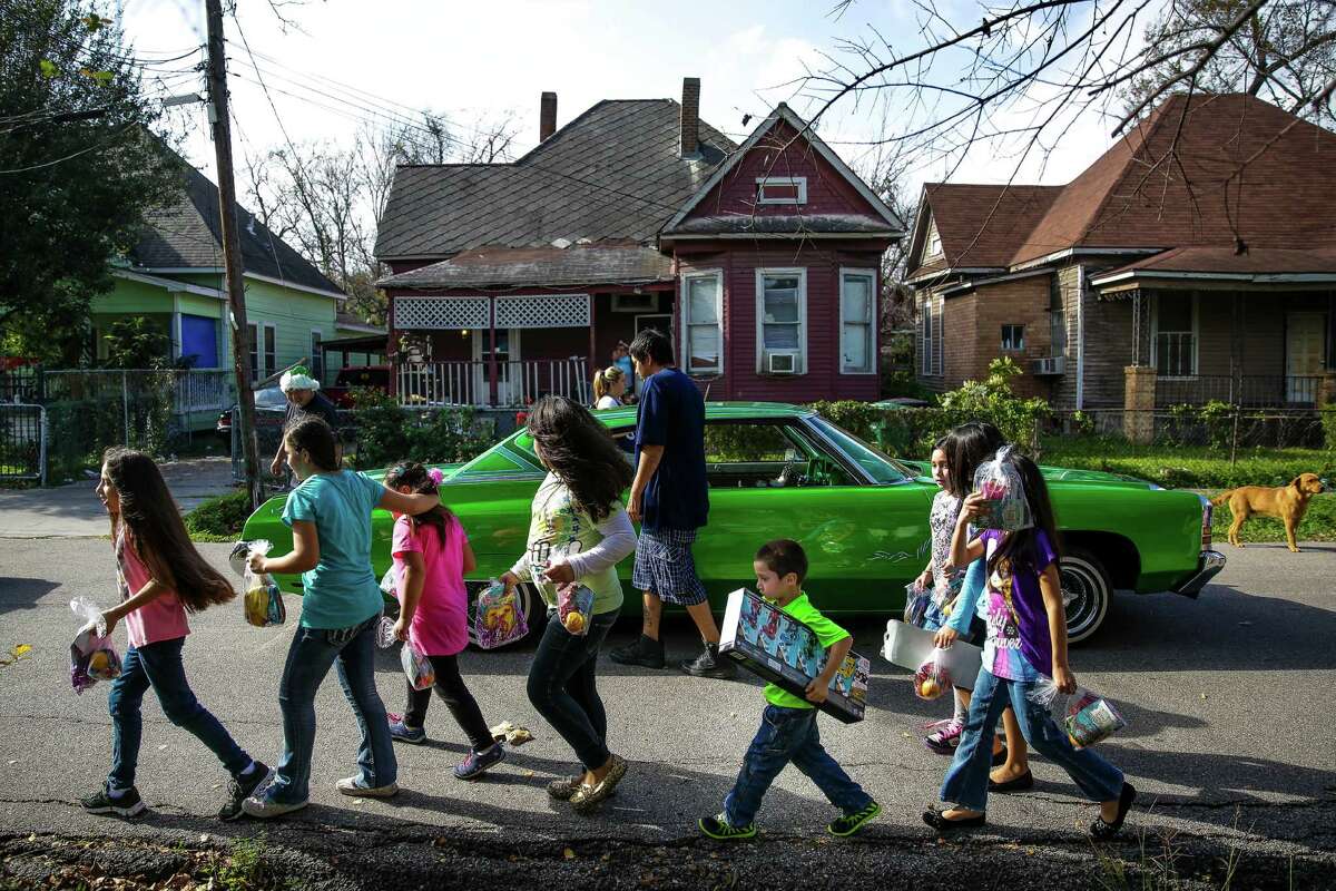 A group of kids walk back to their homes with their new presents from the Latin Fantasy Lowrider Car Club as the club distributes toys and goodie-bags throughout Houston's low-income neighborhoods Friday, Dec. 25, 2015.