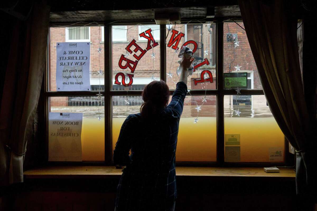 A woman cleans the window inside her wine bar Monday as floodwaters rise from the rivers Foss and Ouse, after they burst their banks in York, England.﻿