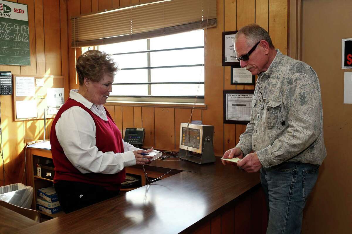 Richard Collier, Zavala County rancher, settles with Josie Prado, secretary at Leona Valley Gin as he picks up a load of cottonseed for deer feed at the gin near Batesville, Texas, Wednesday, Dec. 23, 2015. Collier owns a pipe company that sells to oil drilling companies. With the downturn in the oil business, his sales have dropped.