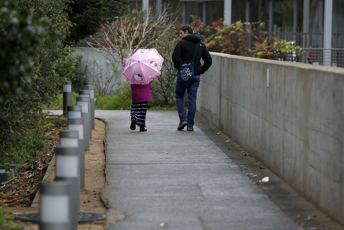 A girl holding a Hello Kitty umbrella walks with her guardian near the California Academy of Sciences building in San Francisco, California, on Sunday, Jan. 3, 2016.