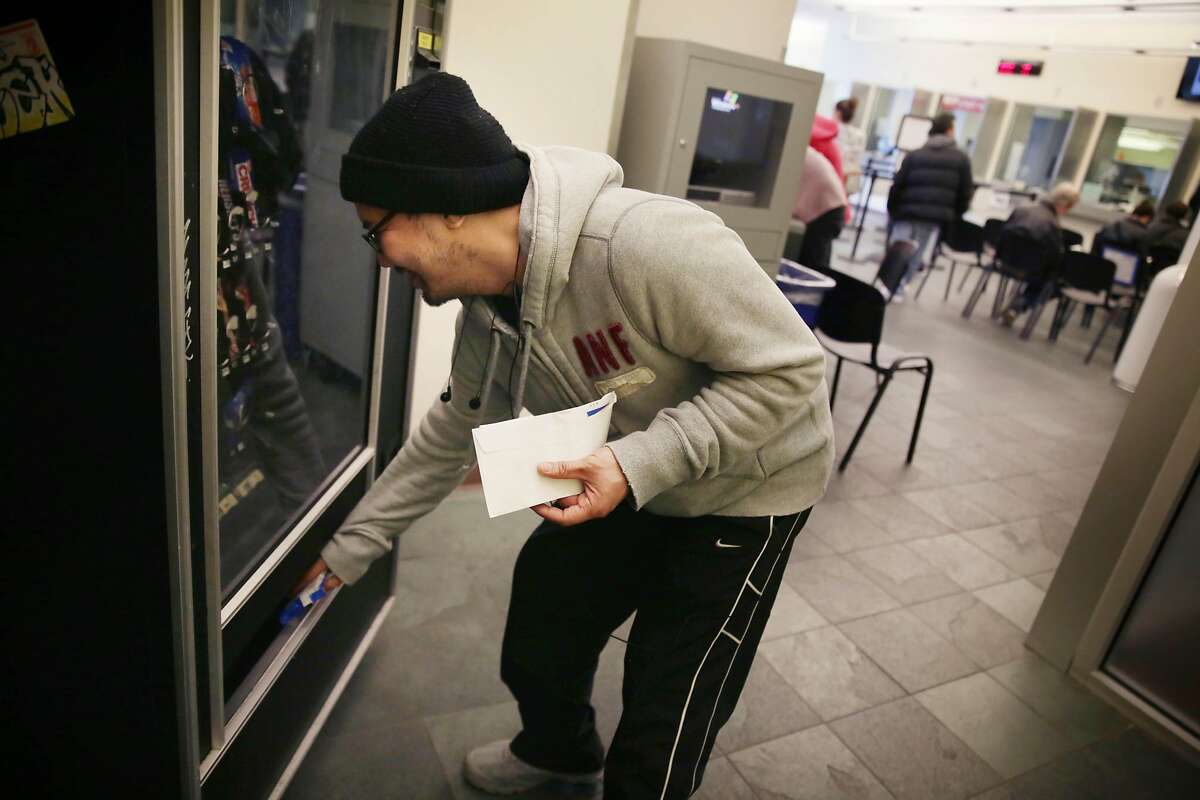 Will Nacor (left) of San Francisco picks up his selection after making a purchase from a vending machine at the SFMTA customer service center on Monday, January 11, 2015 in San Francisco, Calif.
