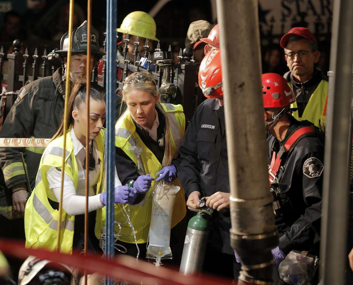 Medical personnel lower an intravenous bag into the hole as Oakland and Alameda County firefighters and emergency personnel worked to free a plumber who was trapped when the hole he was working in collapsed around him in Oakland, Calif., on Tuesday, January 12, 2016.