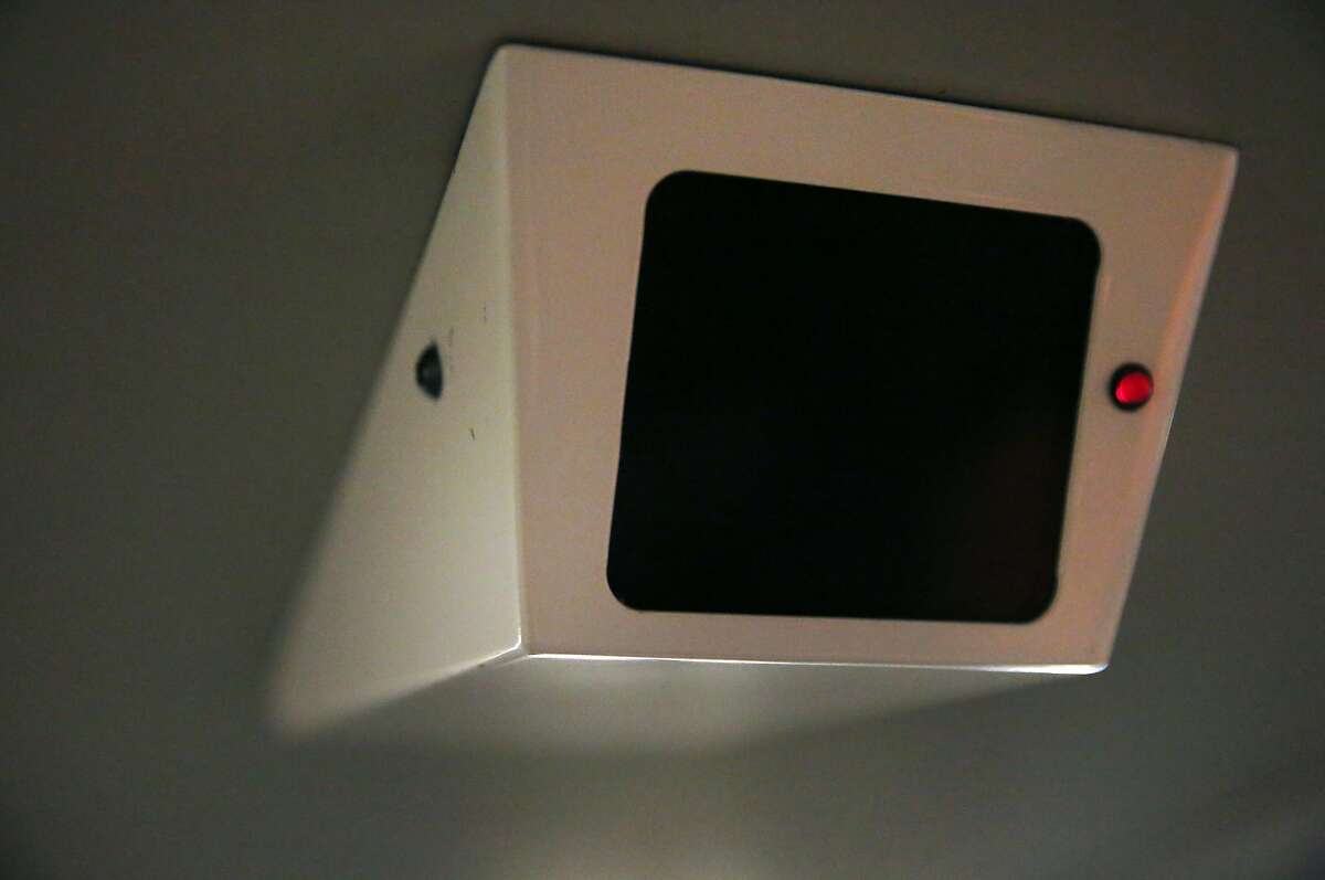 A fake security camera can be seen with a flashing red light as people ride a BART train.