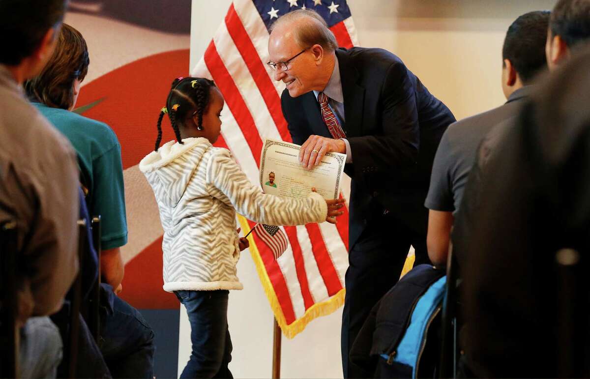 Bexar County Judge Nelson Wolff (right) hands five-and-a-half-year-old Aliya Omar her Certificate of Citizenship as the DoSeum hosts a ceremony in cooperation with U.S. Citizenship and Immigration Services on Saturday, Jan. 16, 2016. 52 children from 24 countries qualified for a Certificate of Citizenship as flags were waved and as guests watched a video message from President Barack Obama. Locally, Bexar County Judge Nelson Wolff spoke at the event and presented the new Americans with their certificates. Immigration services officials said they plan on holding similar events up to four times a year. The local immigration office serves 78 counties in South Central Texas. (Kin Man Hui/San Antonio Express-News)