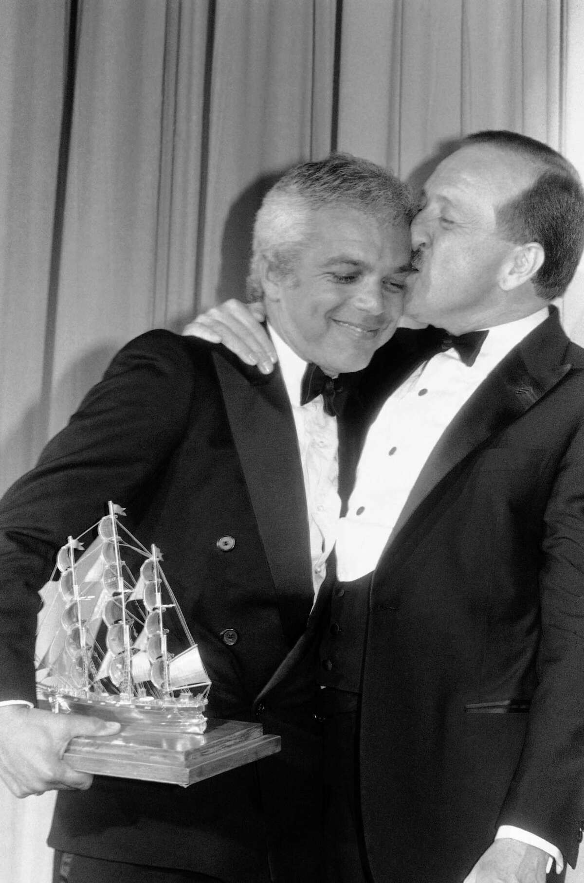 Designer Ralph Lauren gets a kiss from Career Achievement Award presenter Wilkes Bashford during Cutty Sark Fashion Awards ceremonies in Philadelphia, June 21, 1983. Lauren received the award for "continuing leadership and outstanding contributions to men’s fashions." Bashford was last year's recipient of a Cutty Sark award for creative retailing. The winners are selected by a panel of U.S. fashion writers. (AP Photo/George Widman)